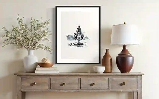 Framed ink print of person on donkey displayed on wooden console table with lamp, vase, and decorative objects.