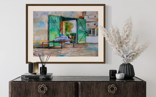 The Corner Shop watercolor art print mockup by Salih Abdo showing framed Sudanese shop scene in modern interior