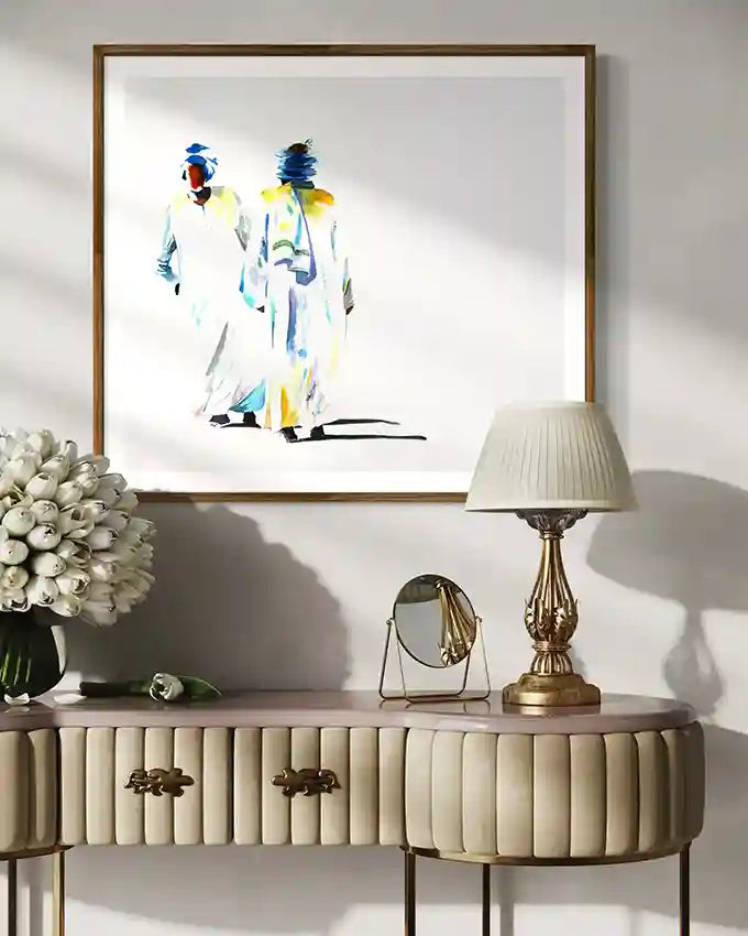 Decorative console table with a lamp, mirror, and flowers against a wall with framed art print by artist "Galal Yousif", UAE