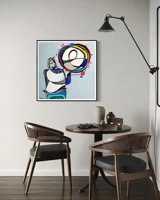 Small dining area with a round table and two chairs, featuring a Print by artist Galal Yousif on the wall.