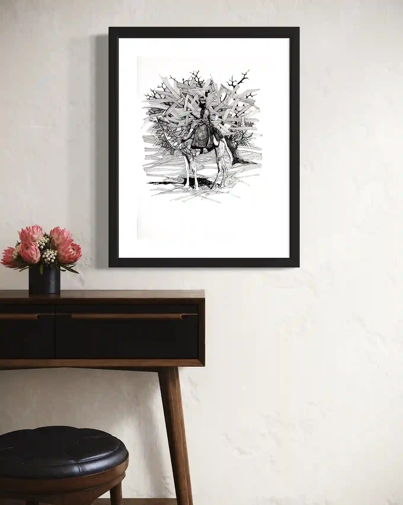 Man From Hajana framed art by Obada Gabir displayed above wooden desk with pink protea flowers in modern interior