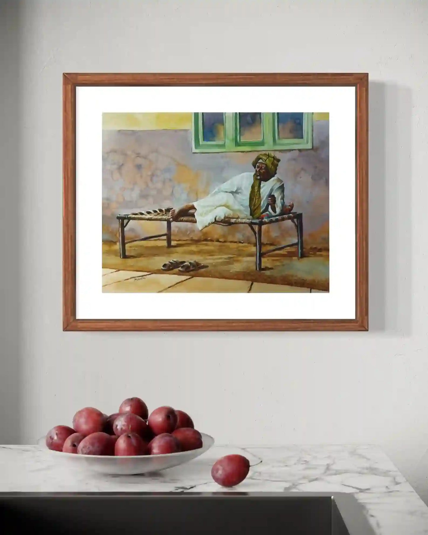 A Quiet Moment watercolor by Hussein Merghani in wooden frame on white wall with red plums on marble counter